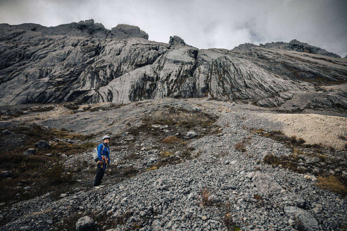 Lone climber traversing barren scree field with mountain walls in distance