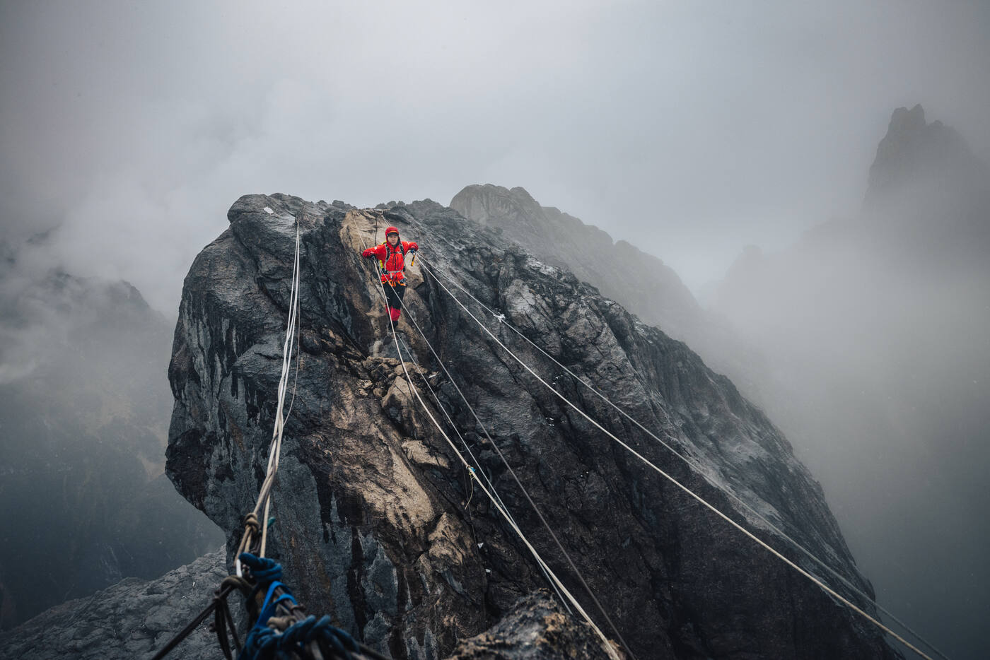 Climbers using fixed ropes, silhouetted against misty mountain background