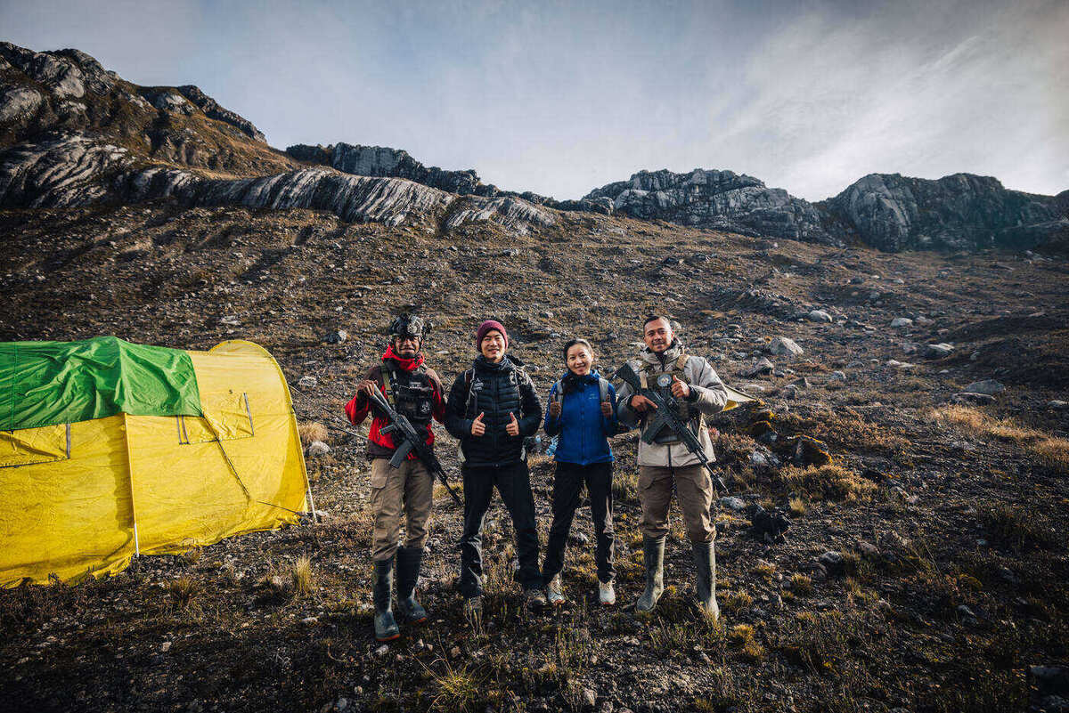 Four people posing beside a yellow and green tent at base camp with limestone ridges behind