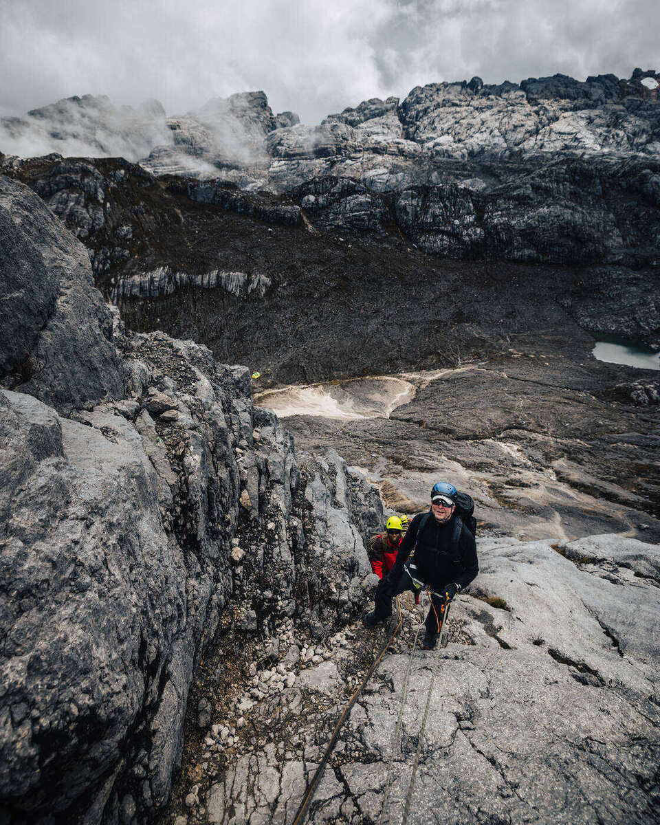 Two climbers on white rock formation with ropes and mountain valley behind