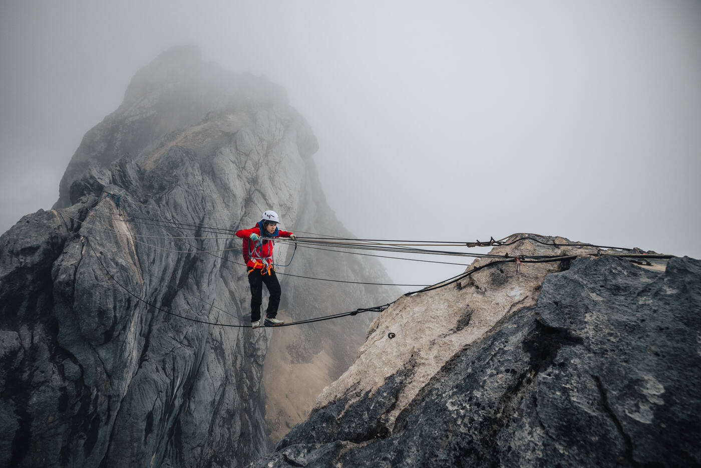 Climber traversing fixed rope stretched between rocky outcrops in misty atmosphere
