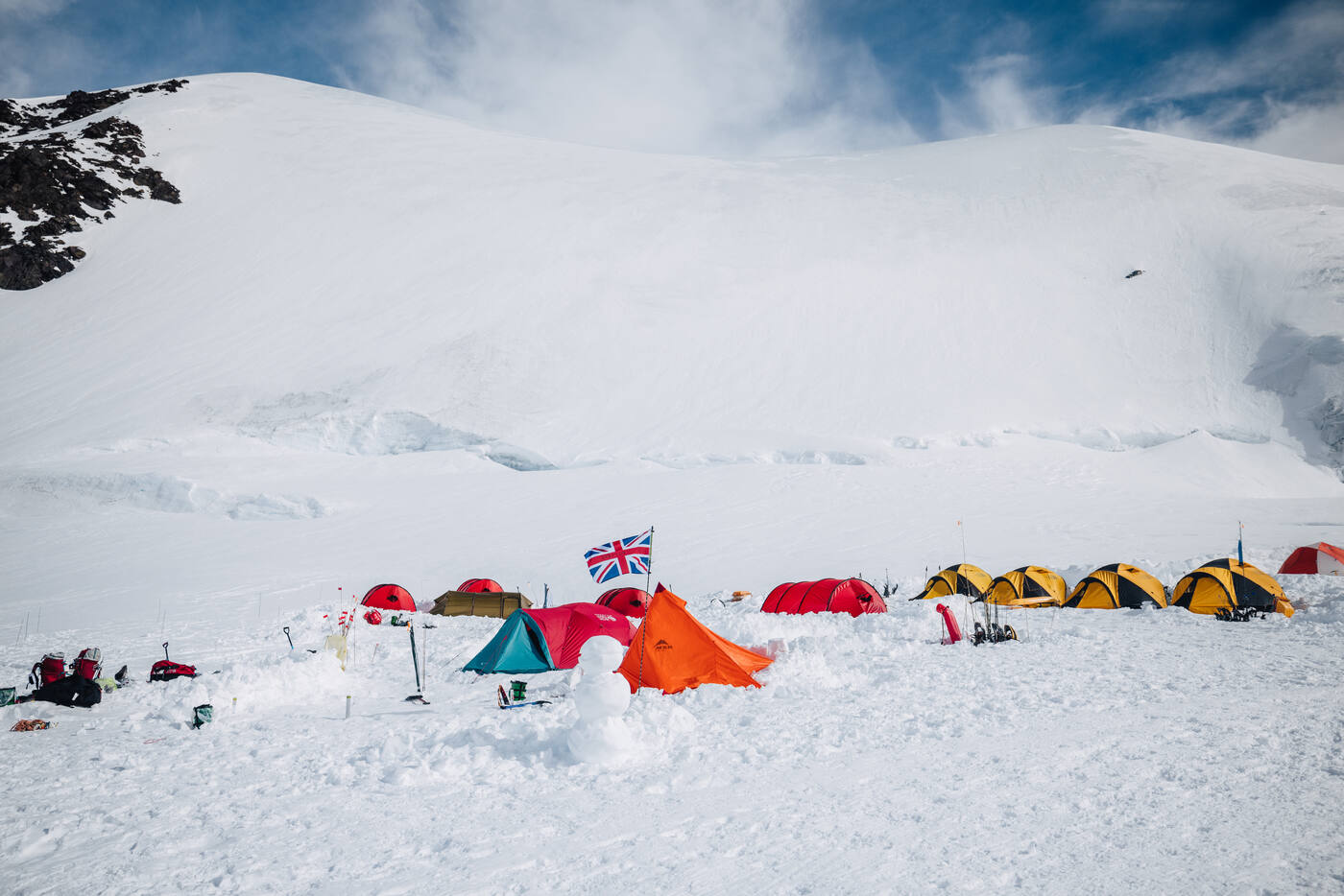 Colorful tents at 11,200 ft camp with a Union Jack flag flying and snow slopes behind