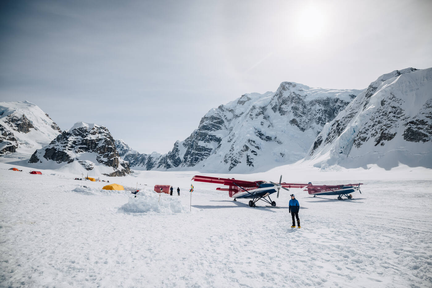 Jason standing at basecamp on the Kahiltna Glacier with bush planes and tents, mountains towering behind