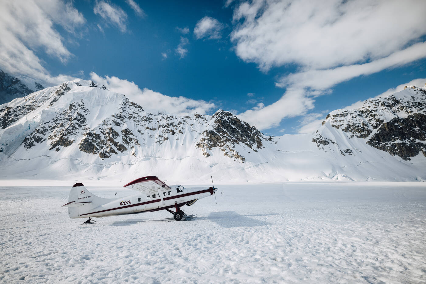 White bush plane parked on the glacier landing strip at basecamp beneath snowy peaks and blue sky
