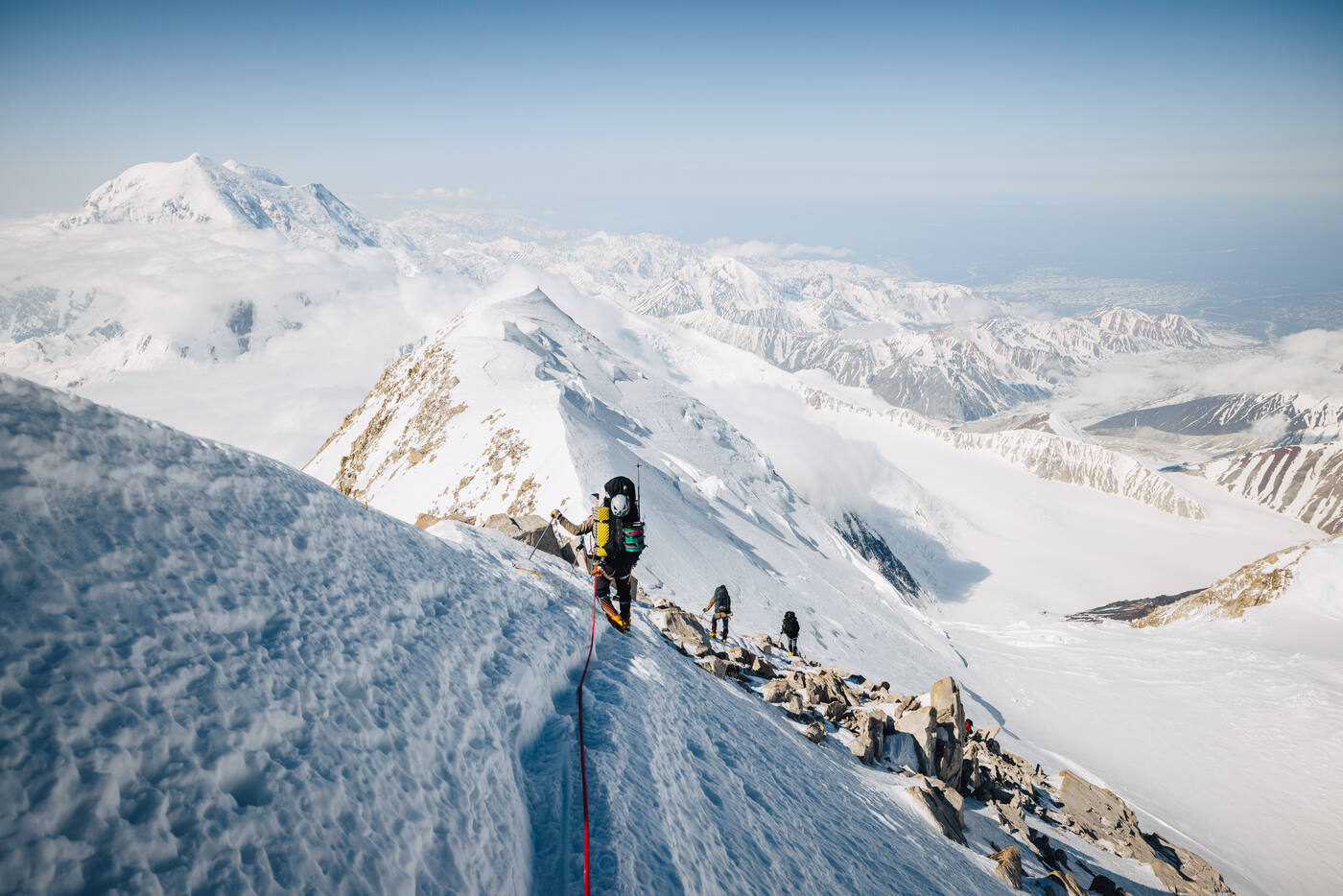 Climber on an exposed rocky ridge high on the mountain with peaks and glaciers far below