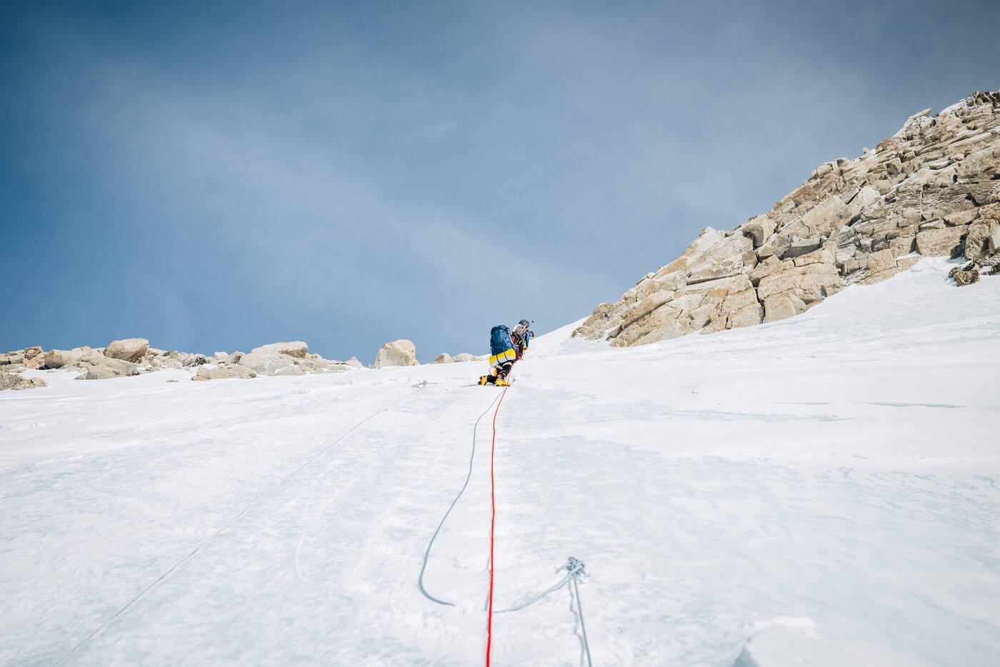 Solo climber ascending a steep snow and ice slope on fixed lines with rocky cliff face above