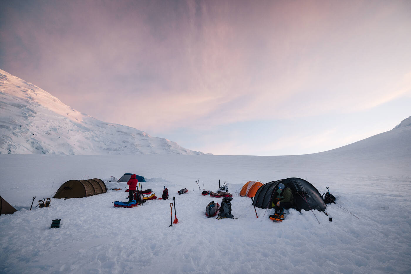 Camp at dawn with tents and sleds scattered across the glacier, pink sky overhead