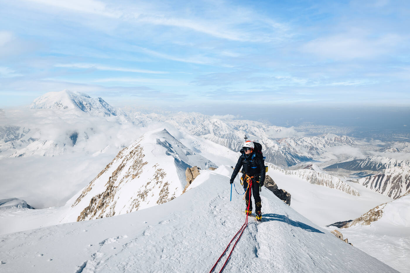 Climber descending narrow snowy ridge with panoramic Alaska Range views