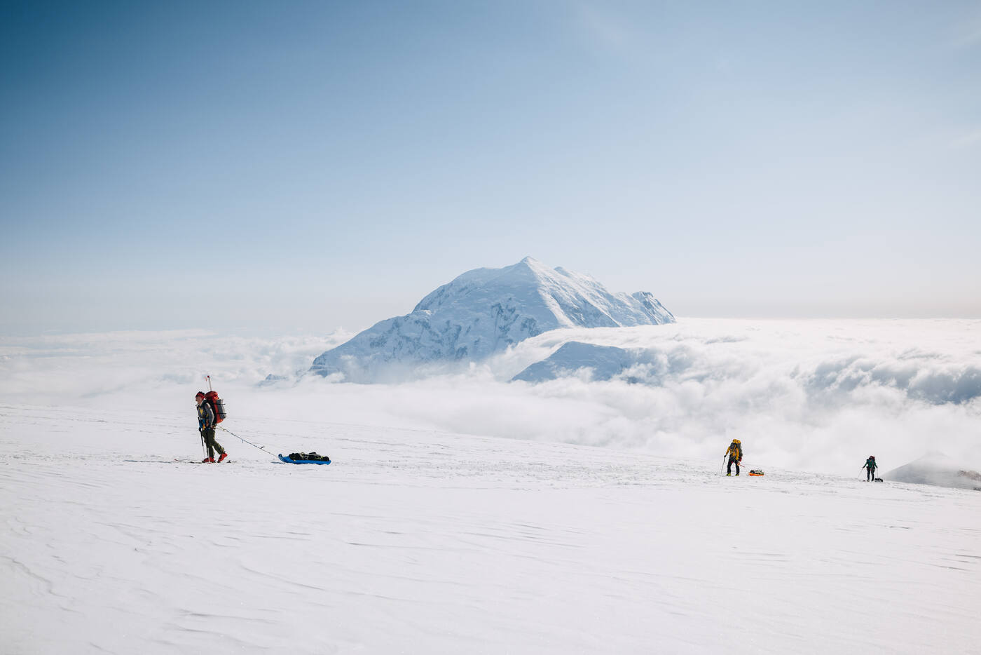 Climbers hauling sleds across a glacier high above the clouds on Denali