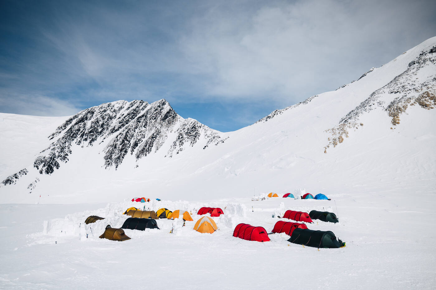 Colorful tents at 17,200 ft high camp surrounded by snow walls with rugged peaks behind