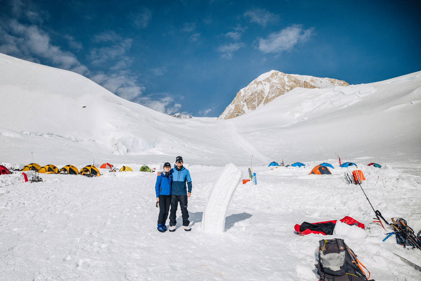 Jason and Grace posing together at 11,200 ft camp with colorful tents and ice seracs behind