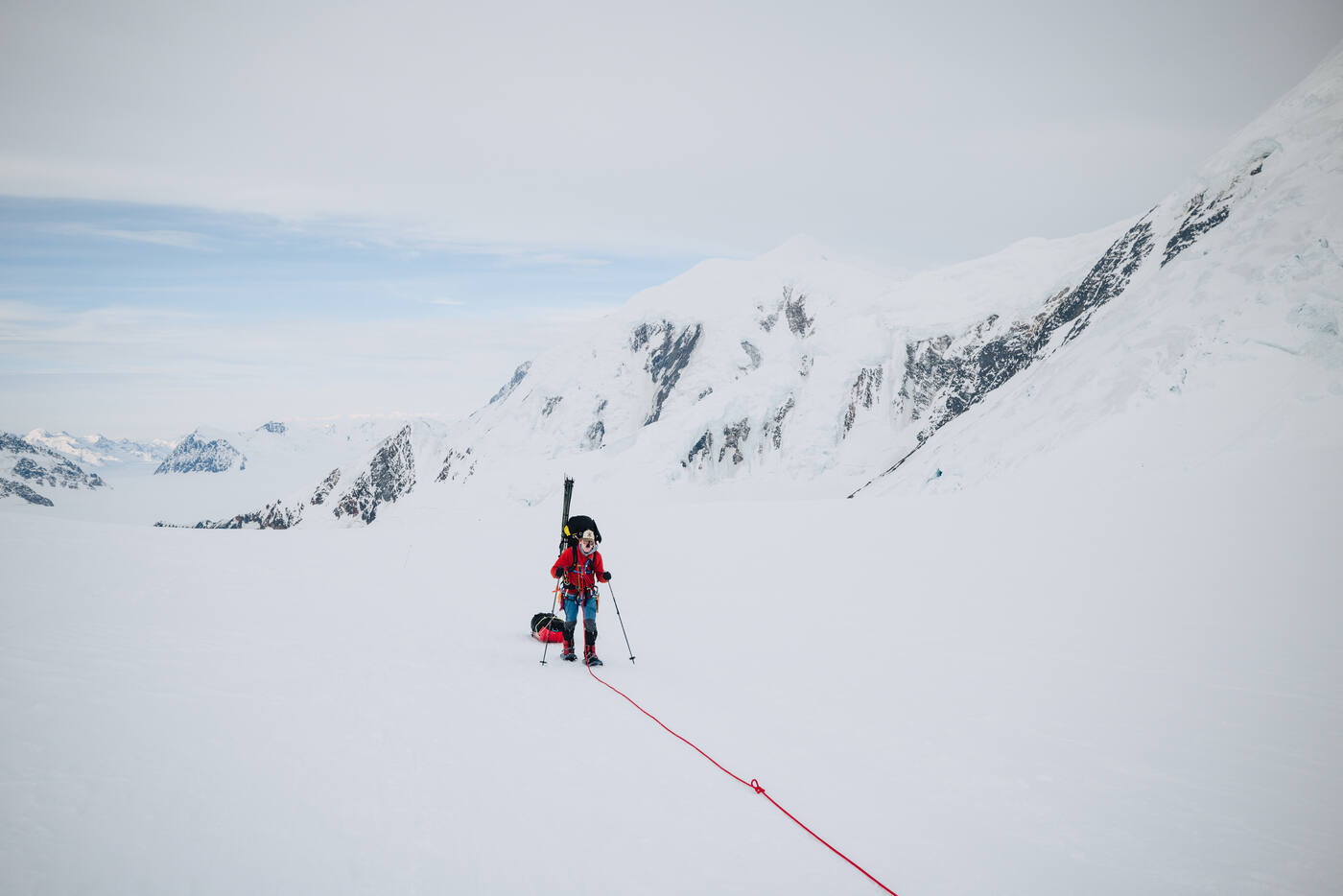 Roped climber hauling a sled up a gentle snow slope with rocky buttresses behind