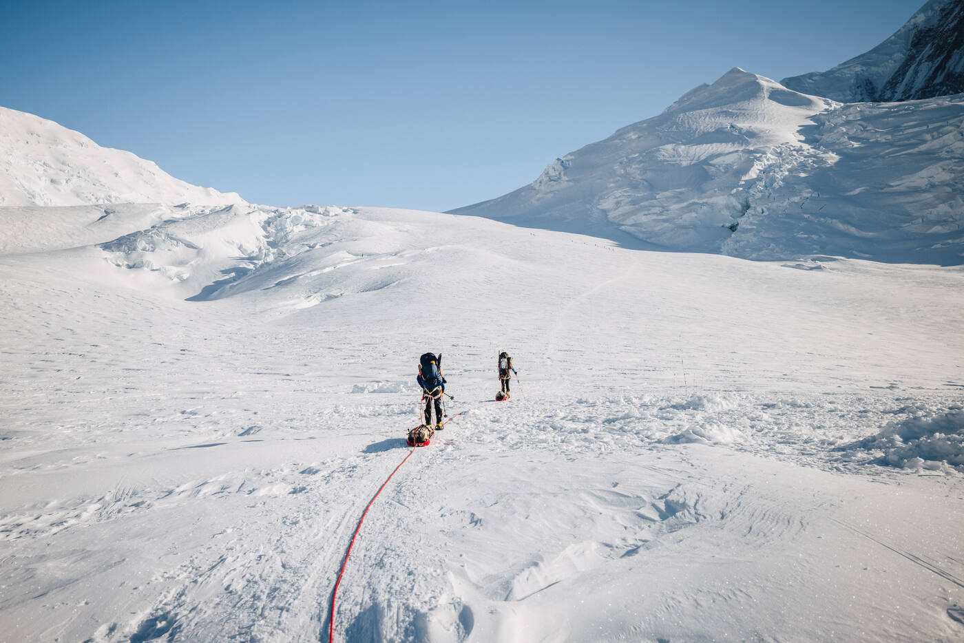 Two climbers roped together ascending a vast white glacier with peaks behind