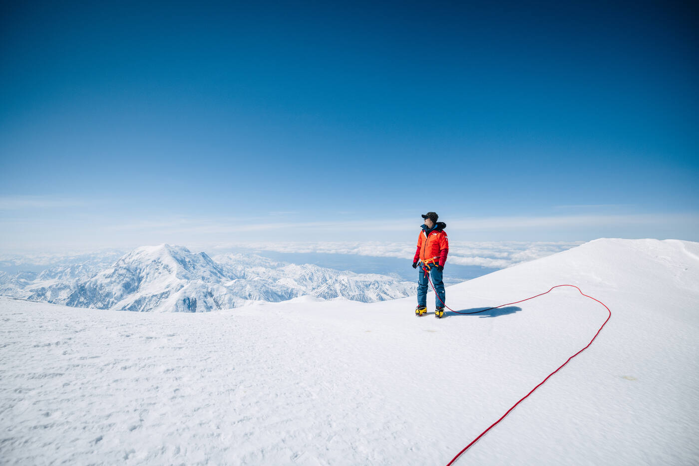 Climber on summit ridge with vast Alaska Range panorama stretching to the horizon