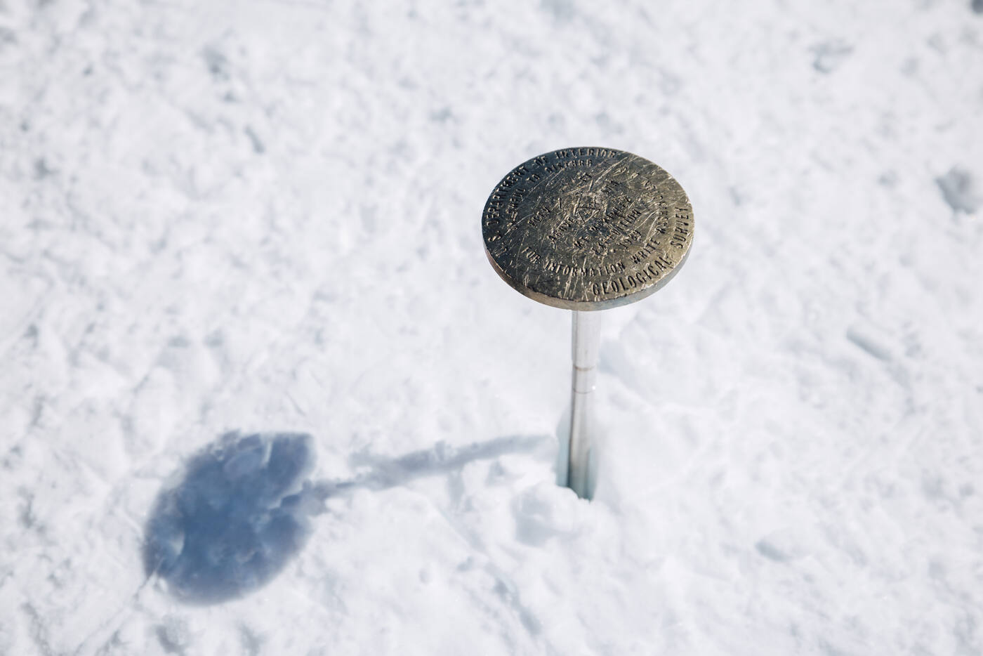 Close-up of a brass survey marker planted in the snow at the summit