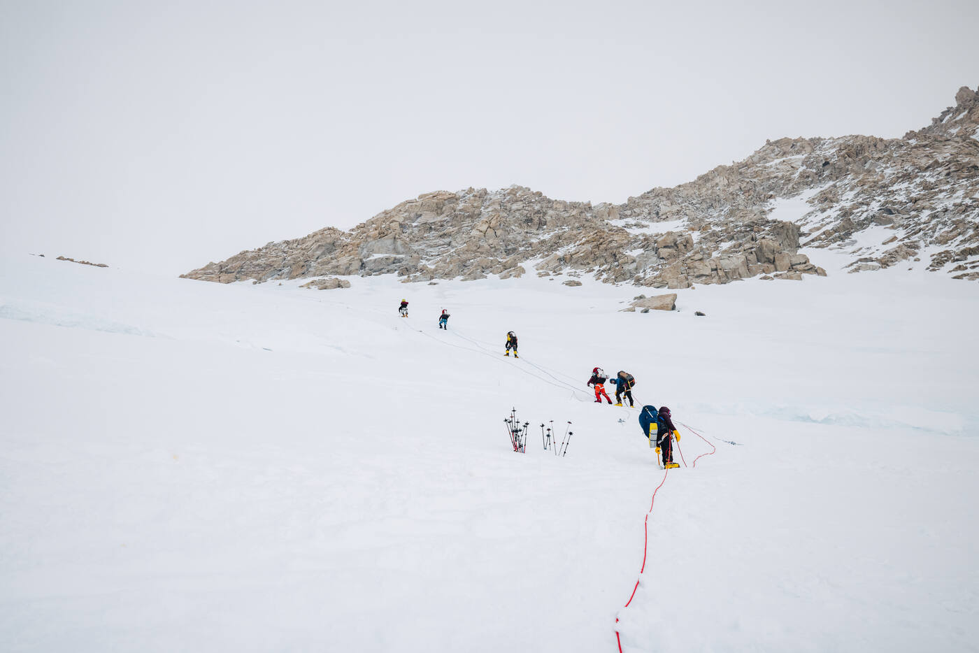 Team of climbers ascending toward rocky terrain on fixed lines