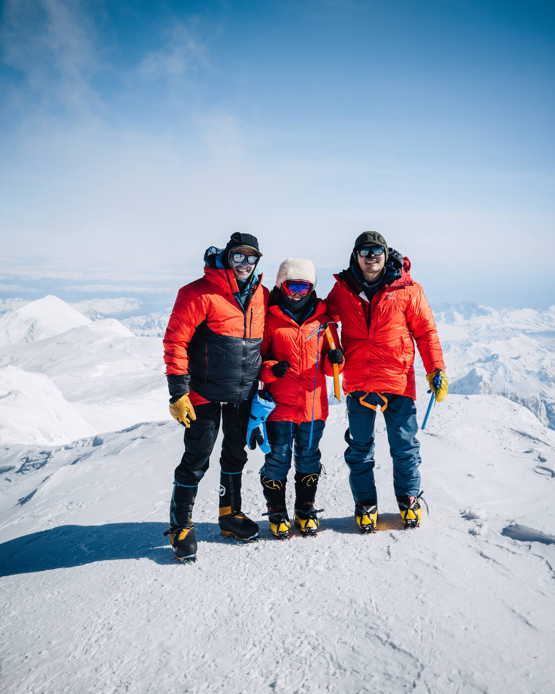 Three climbers standing together at the summit of Denali with full mountaineering gear