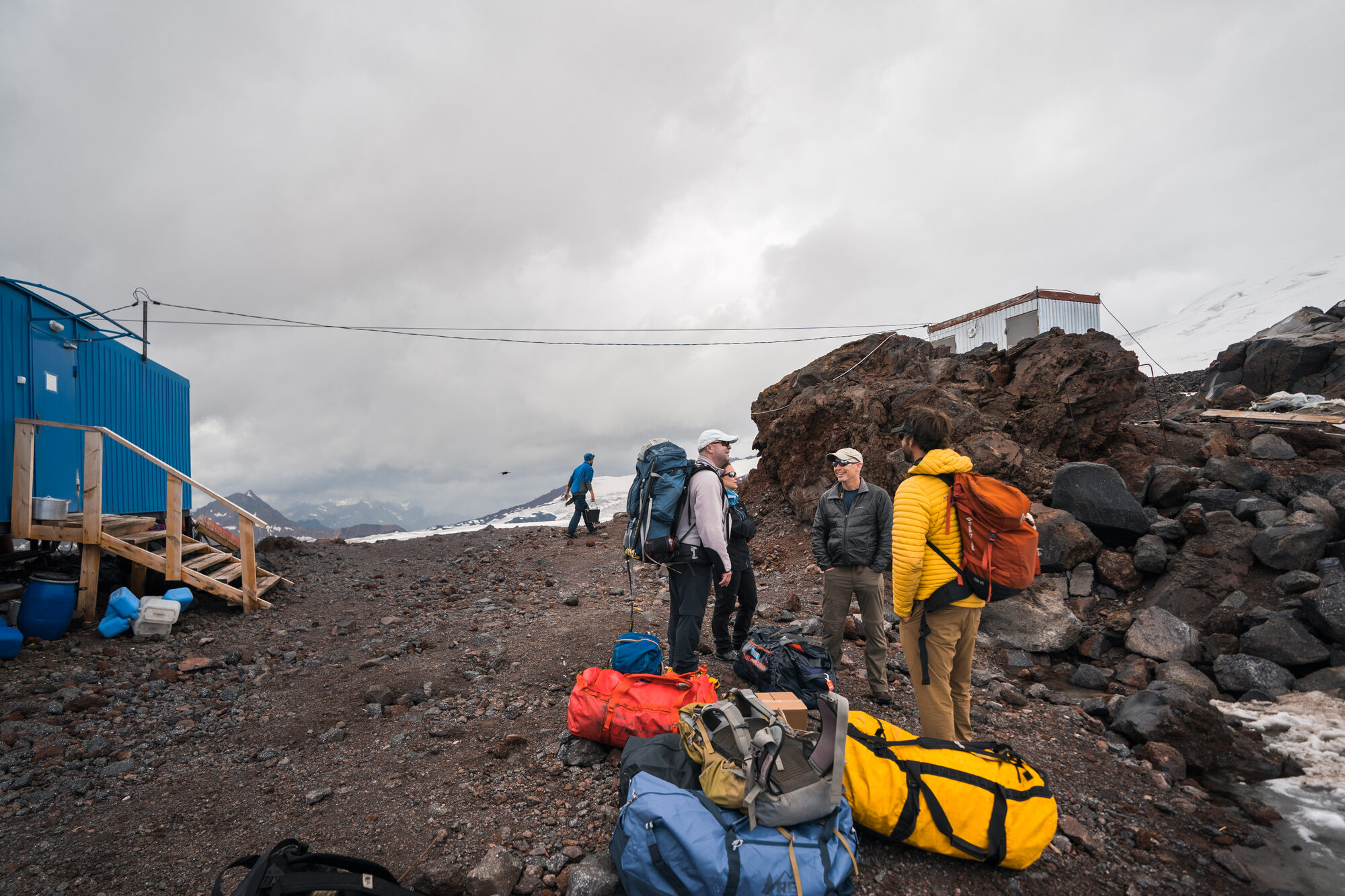 Team arriving at base camp with duffle bags piled up next to the blue container hut