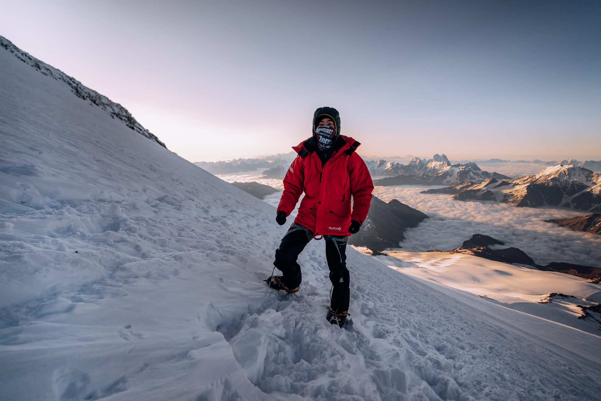 Climber in red jacket ascending steep snowy slope at sunrise on Elbrus