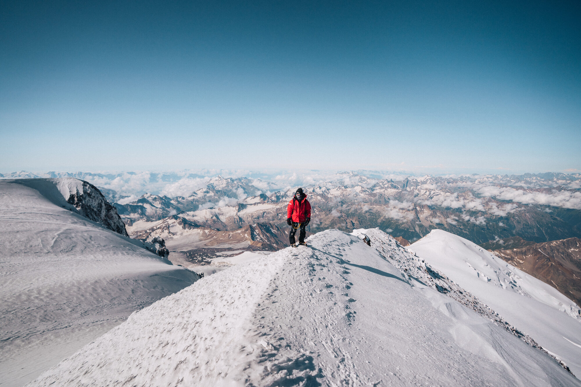 Climber standing on the summit ridge of Elbrus with 360-degree Caucasus panorama