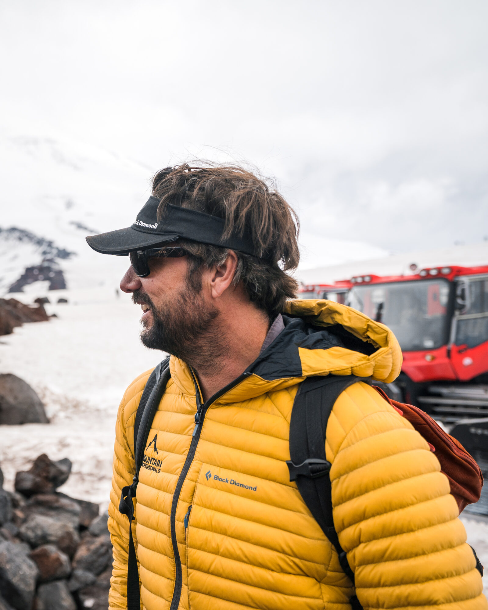 Portrait of a climber in a yellow Mountain Professionals jacket with the red snowcat parked behind