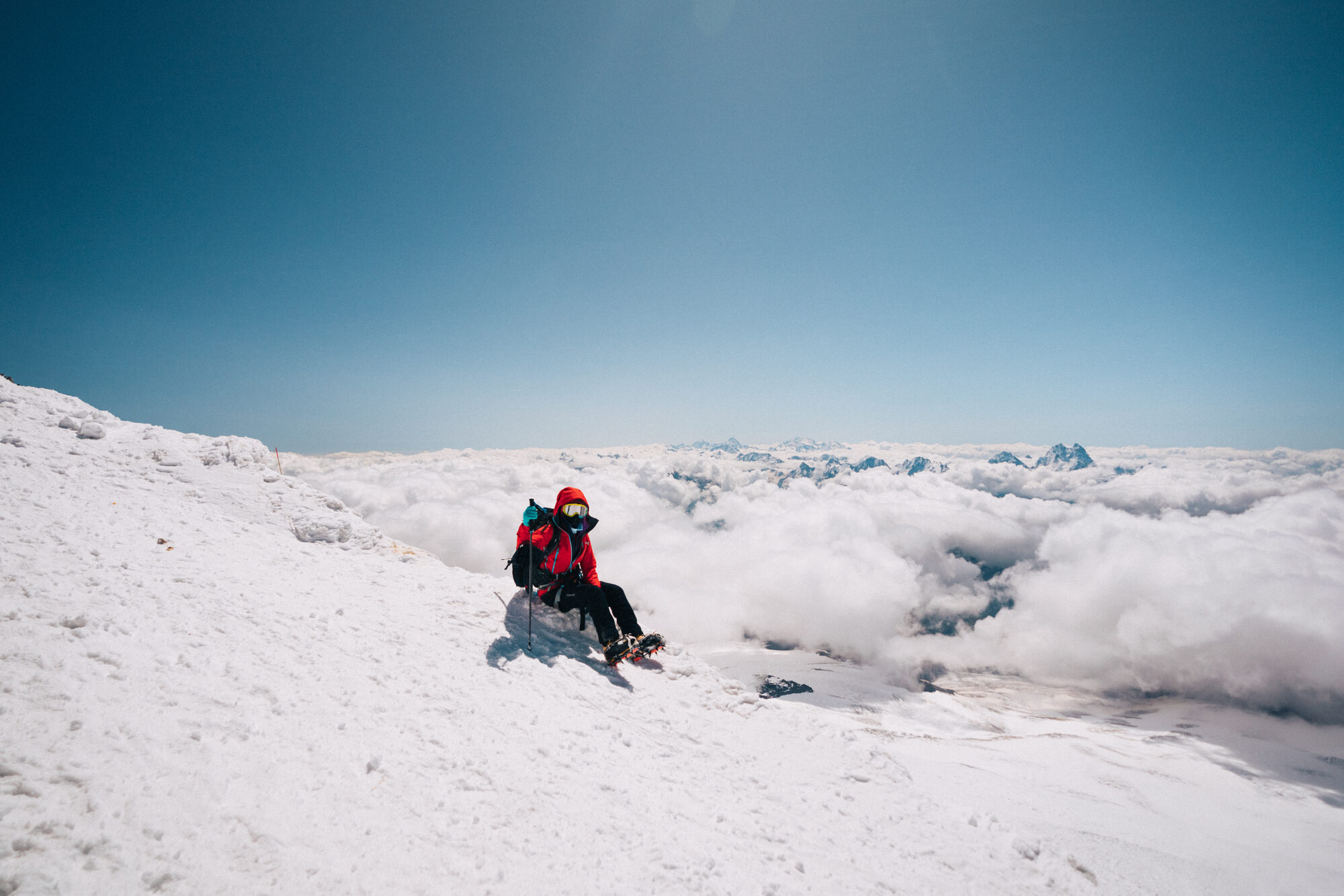 Climber seated on the snow slope above a sea of cloud with peaks poking through