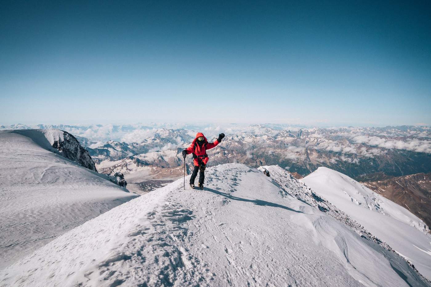 Grace on the Elbrus summit ridge, waving with the Caucasus panorama behind her