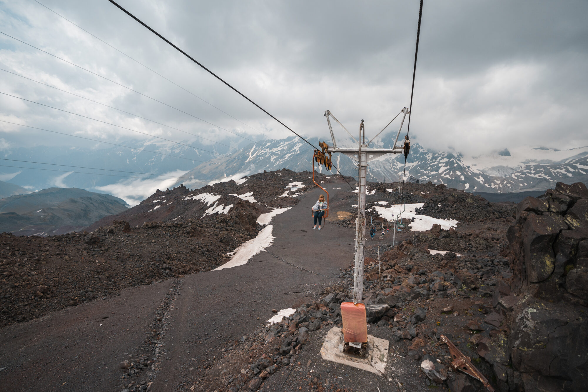 Person walking along a paved path near old ski lift infrastructure on Elbrus with mountains behind
