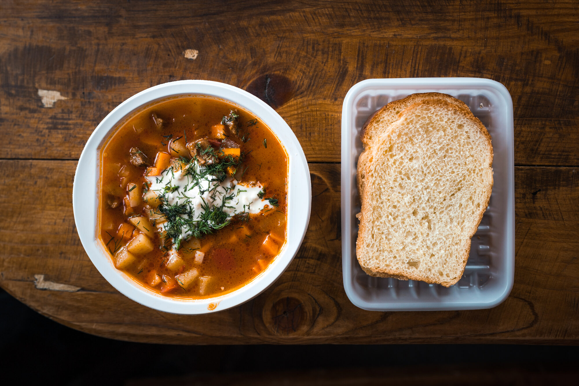 Bowl of hot Russian soup alongside a slice of white bread on a wooden table