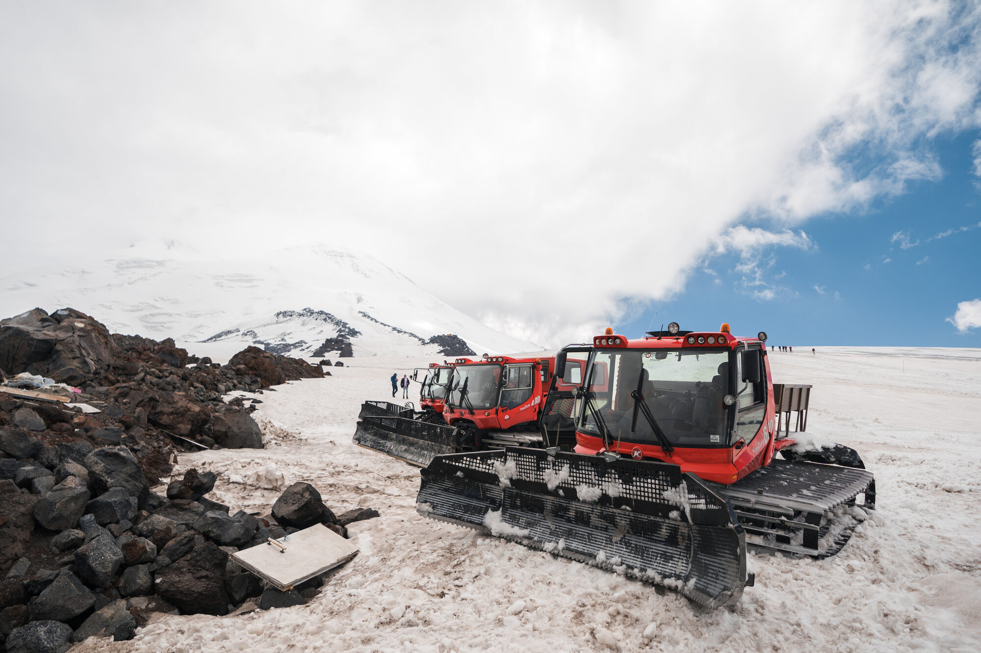 Red snow cats parked on the snowy slopes of Elbrus with the twin peaks behind