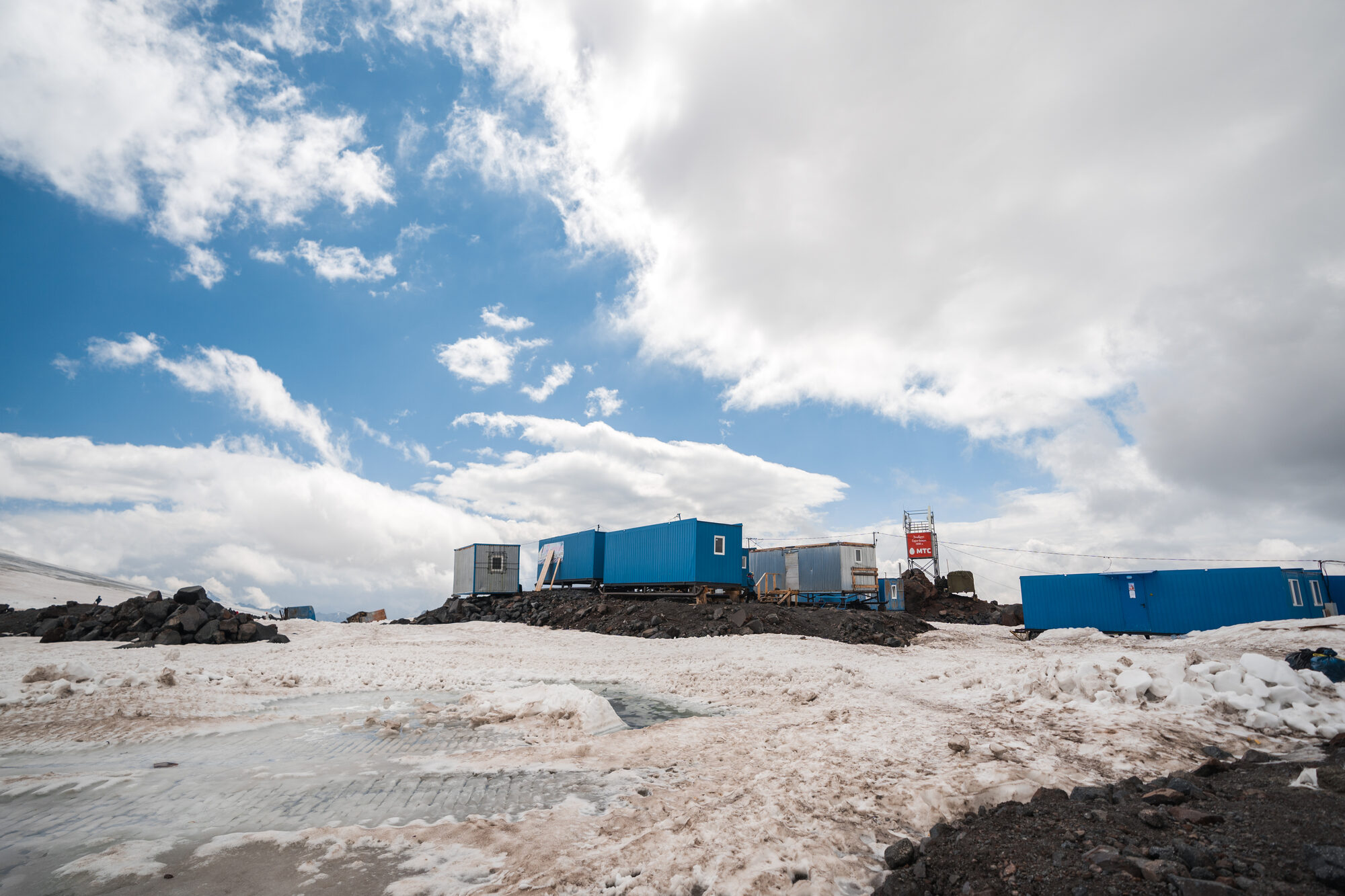 Blue shipping container huts at Elbrus base camp with snow and clouds