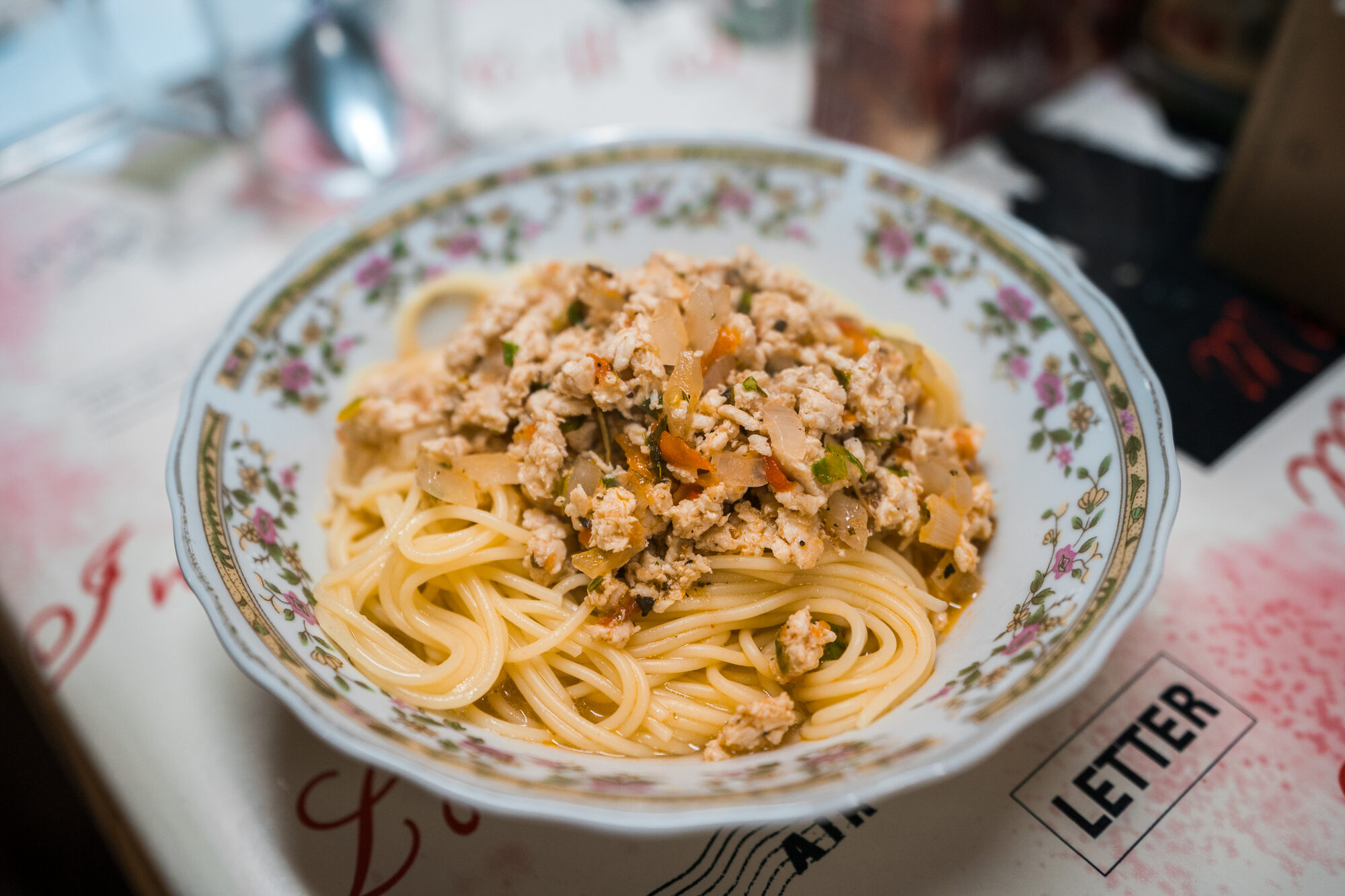 Bowl of spaghetti topped with chicken ragu on a flowered plate