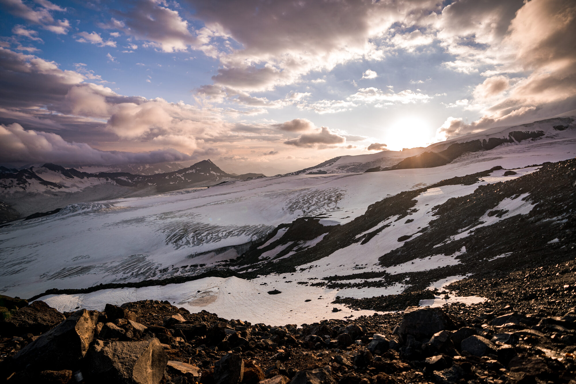 Sun breaking through cloud over the glacier and Caucasus peaks at sunset