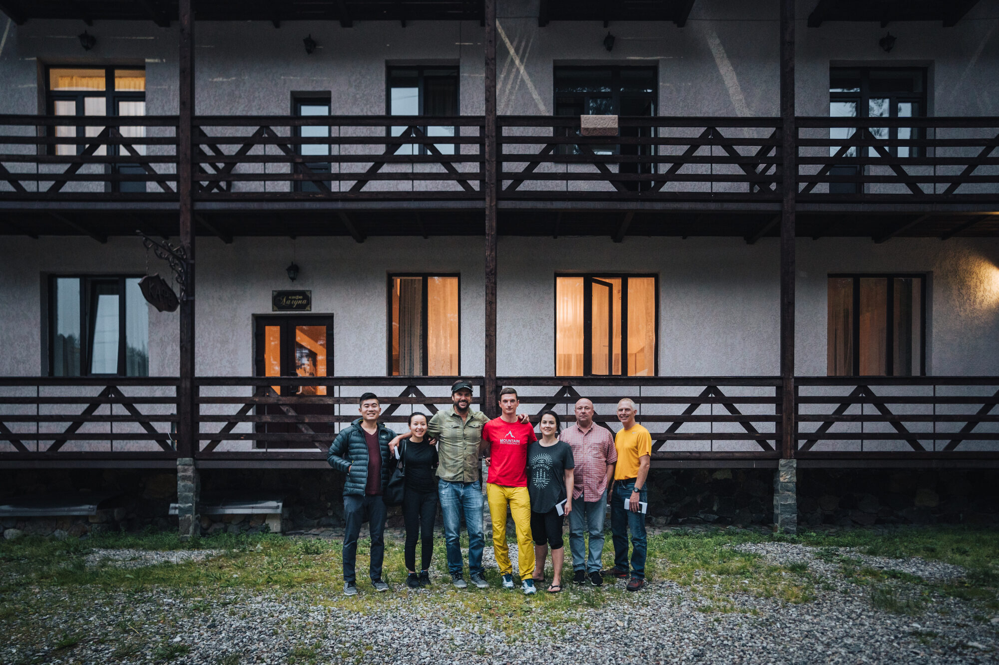 The full climbing team posing outside the wooden lodge in Terskol village in the evening
