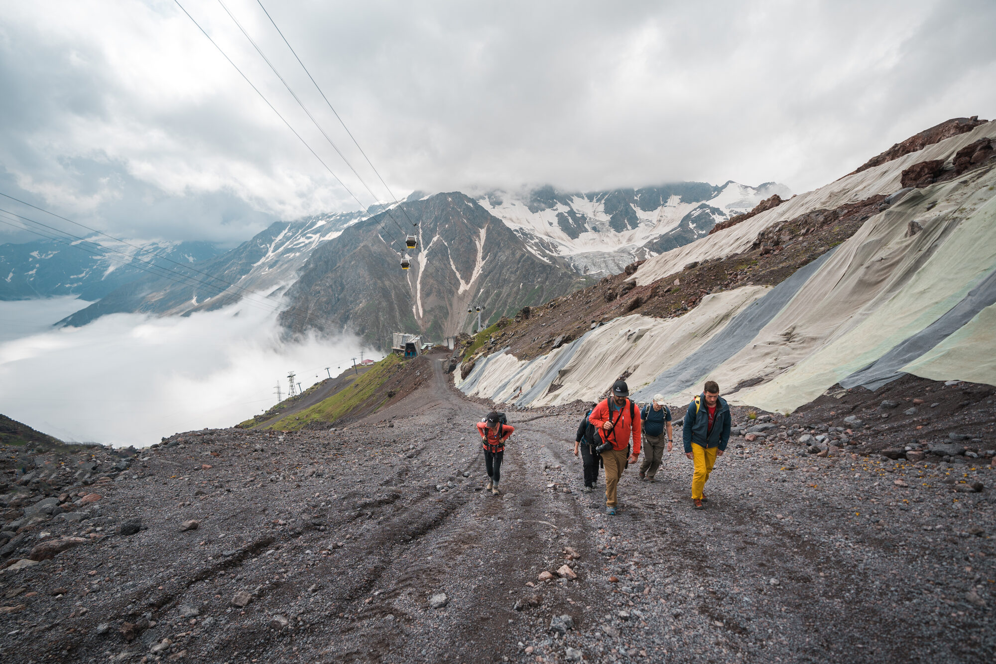 Team hiking up Elbrus gravel slopes with cable car and glaciers visible