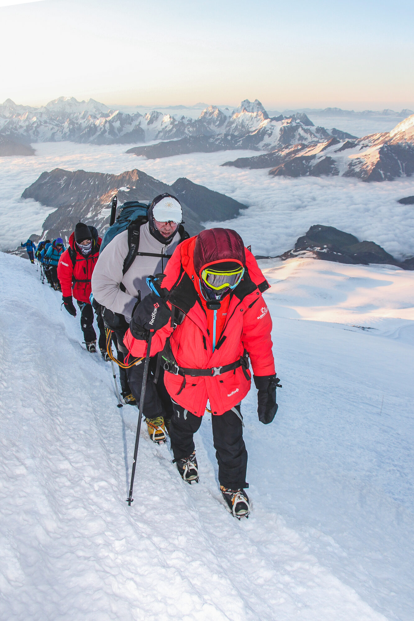 Line of climbers ascending Elbrus at sunrise with mountain panorama