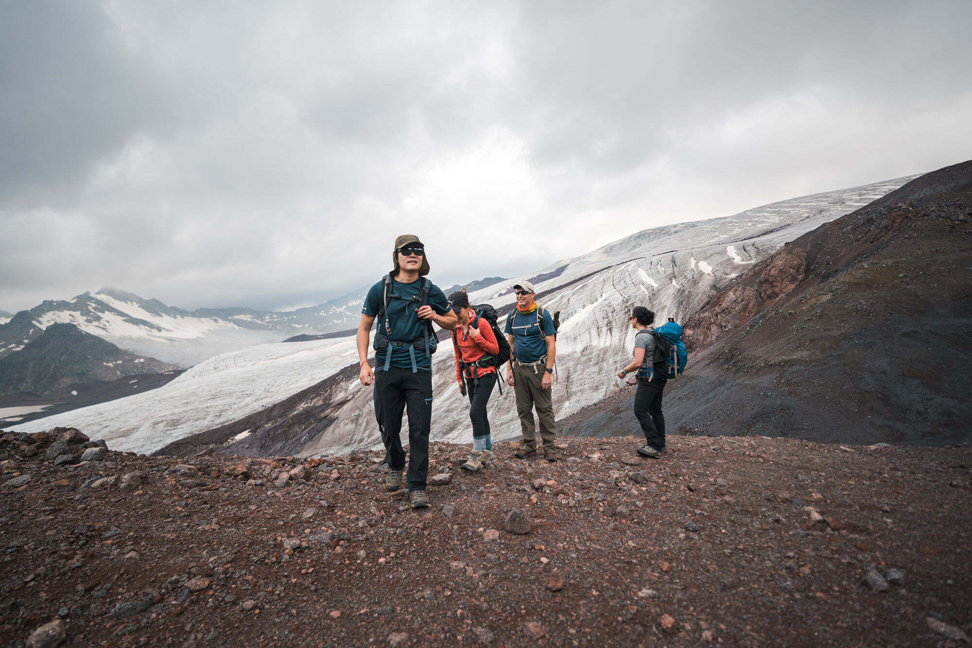 Four climbers standing on the volcanic ridge with a huge wall of glacier ice rising behind them