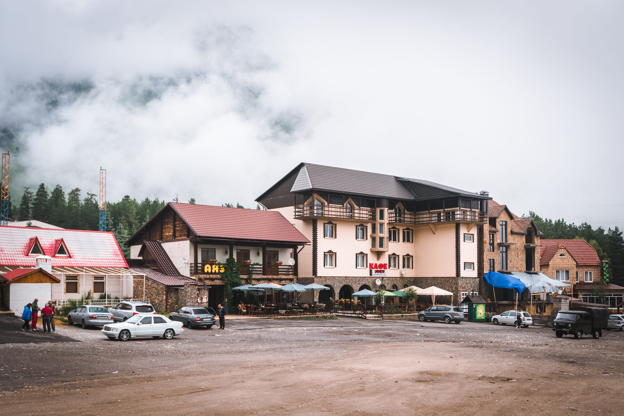 Hotels and cafes around a gravel square in Cheget village under low cloud