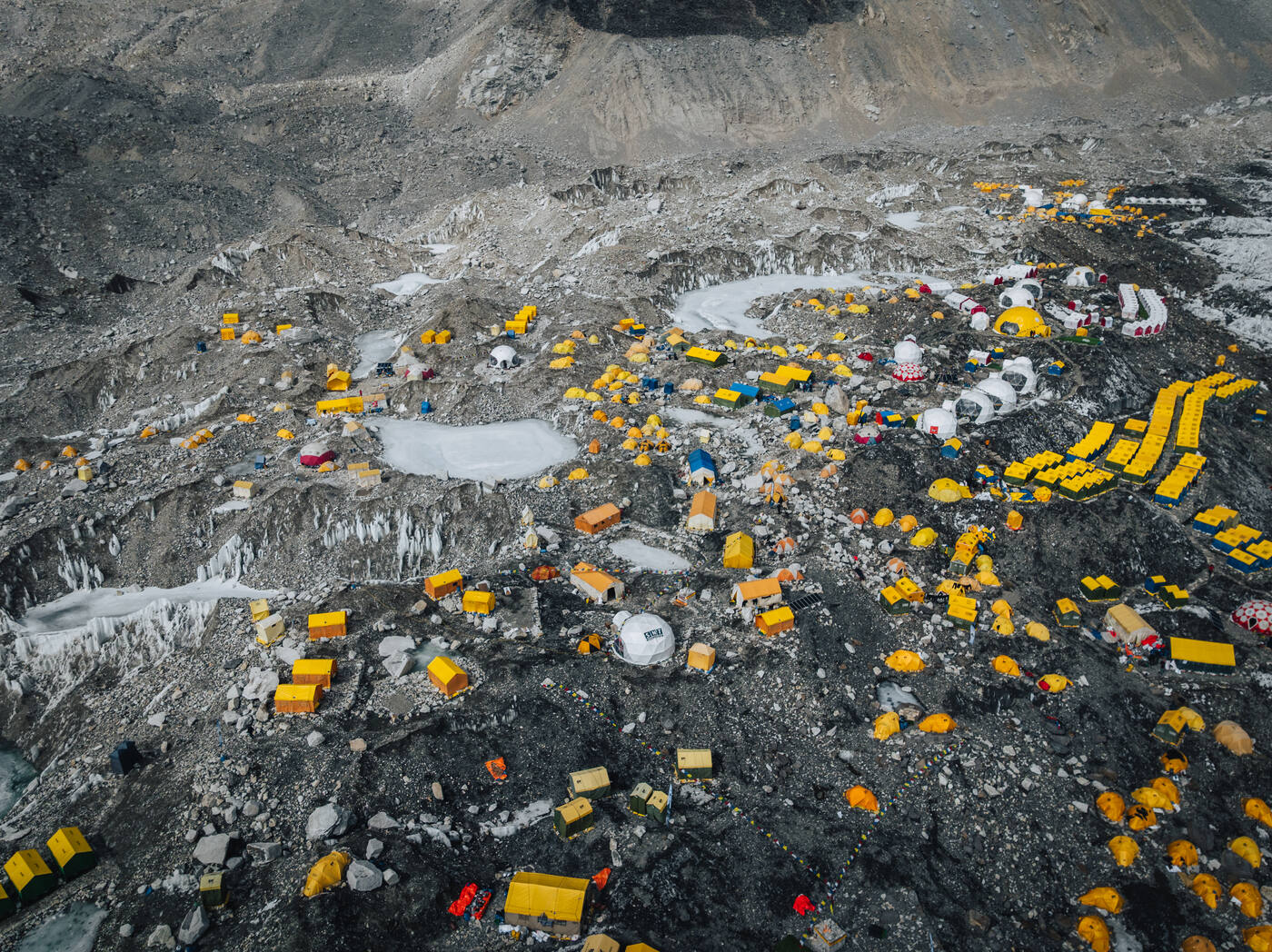 Aerial view of hundreds of yellow and white tents at Everest Base Camp on the rocky glacier