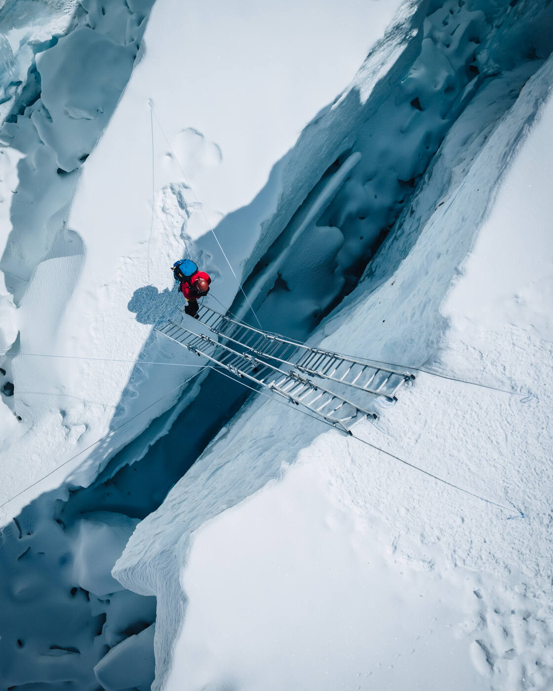 Aerial view of a climber crossing a ladder over a deep crevasse
