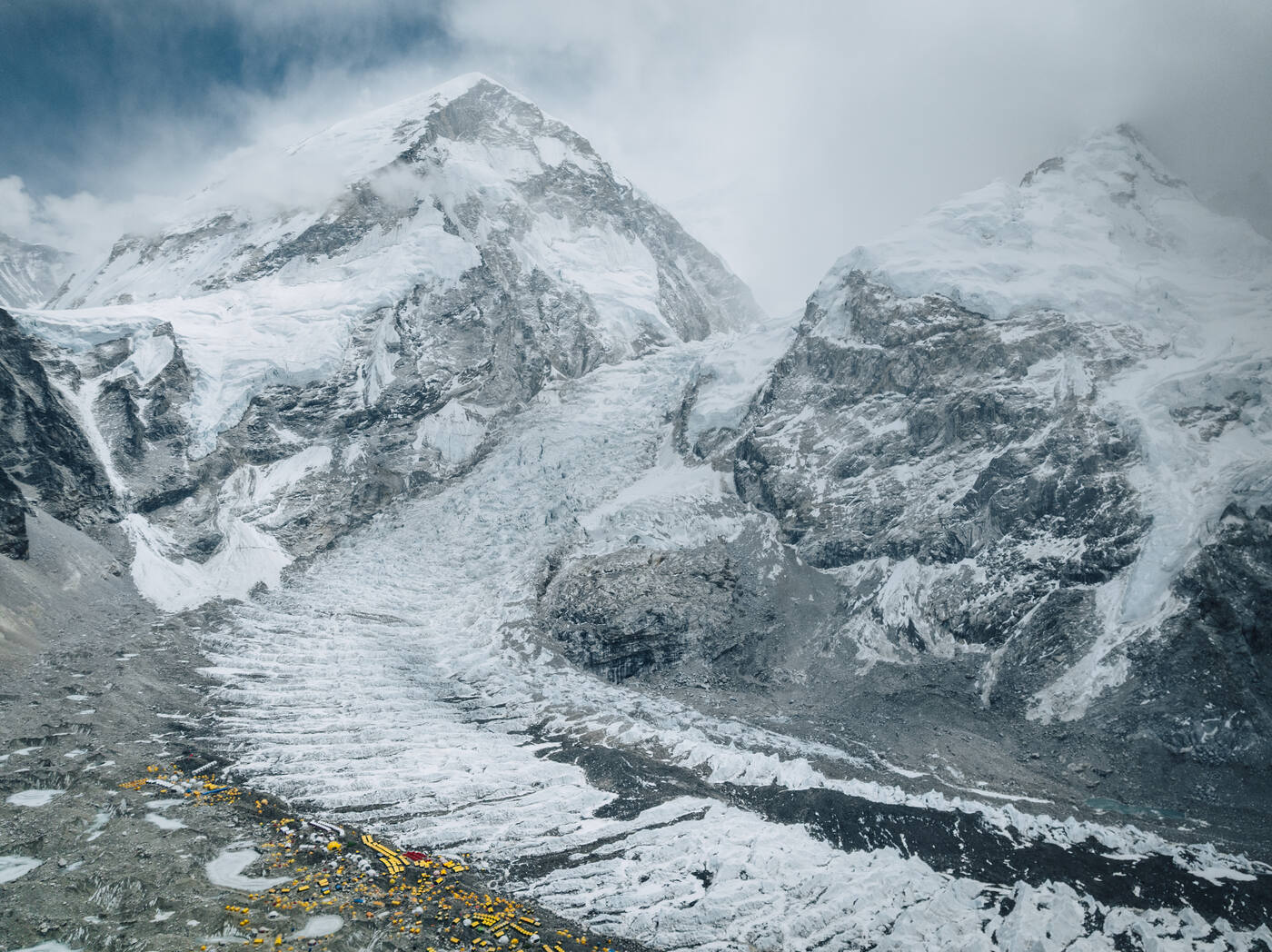 Aerial view of the Khumbu Icefall beneath cloud-covered slopes with Base Camp tents at its foot