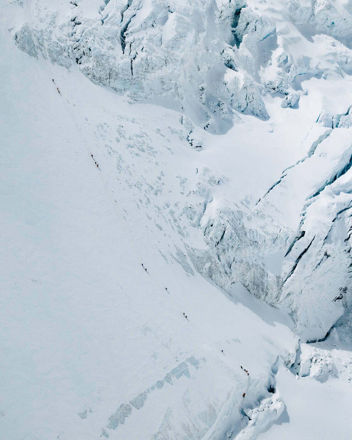 Aerial view of a steep icy face with a line of tiny climbers