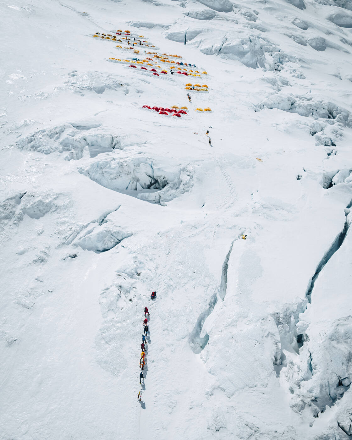 Aerial view of tents on the steep crevassed slope of the Lhotse Face with a line of climbers below