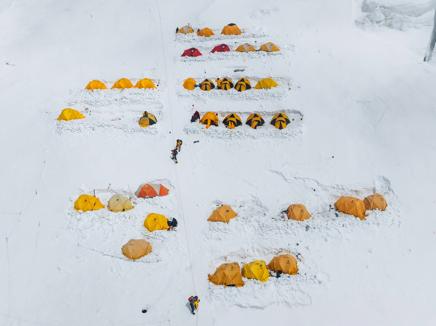 Aerial view straight down on rows of yellow and red tents on snow