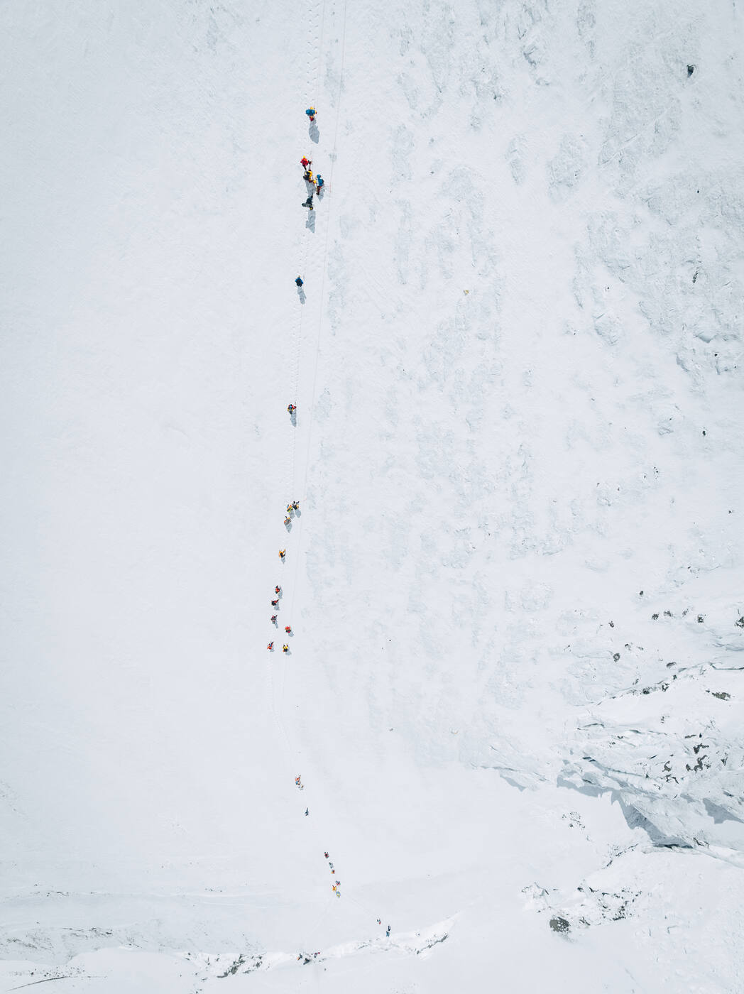 Aerial view of a long line of climbers ascending a snow face