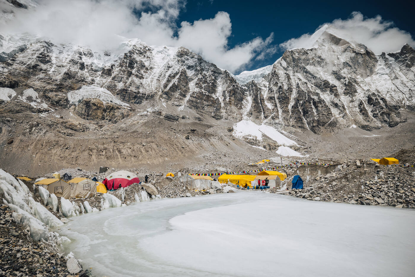 Tents of Everest Base Camp gathered around a frozen glacial pond beneath towering Himalayan peaks