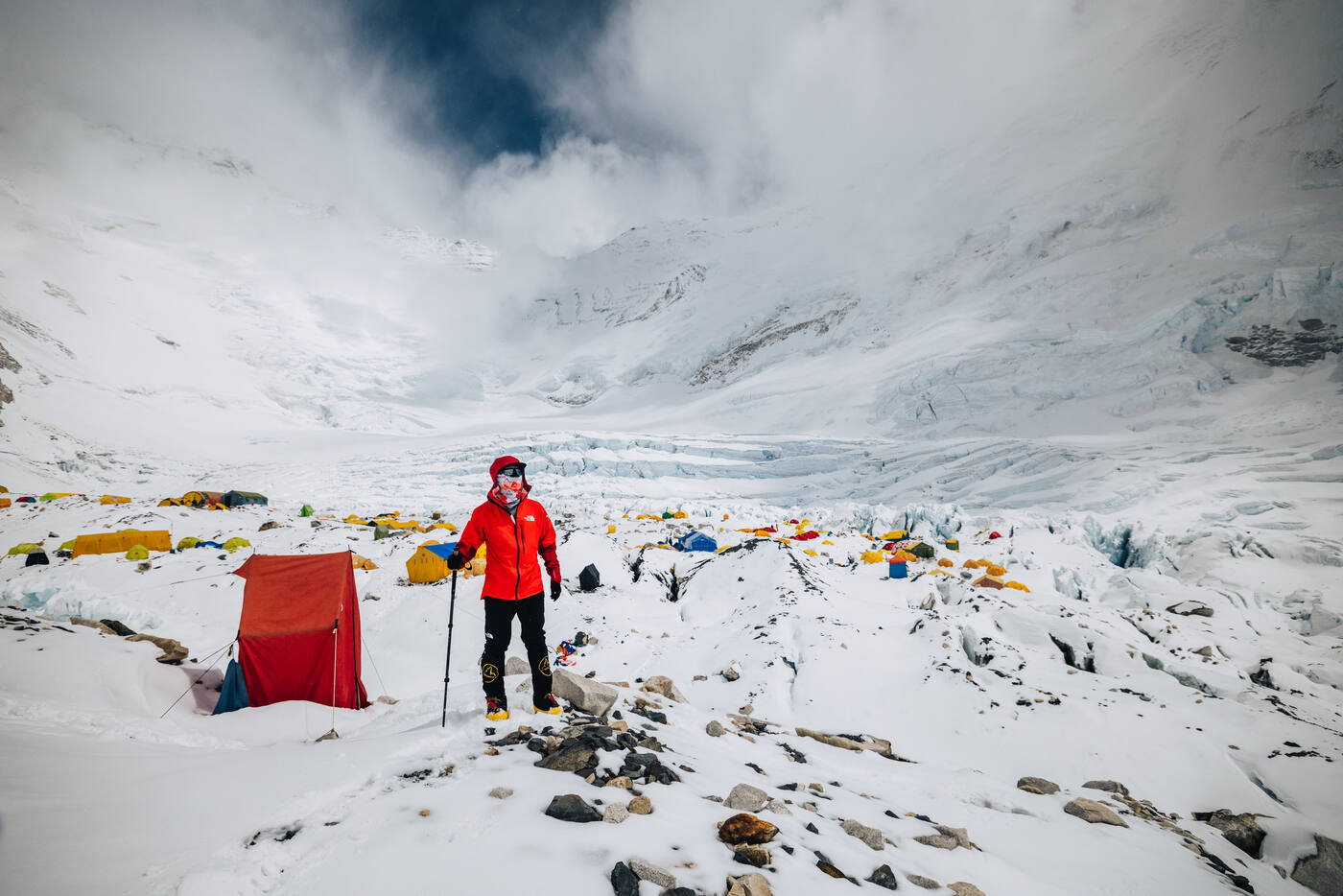 A climber in a red jacket standing among tents at Camp 2 with the Lhotse Face behind