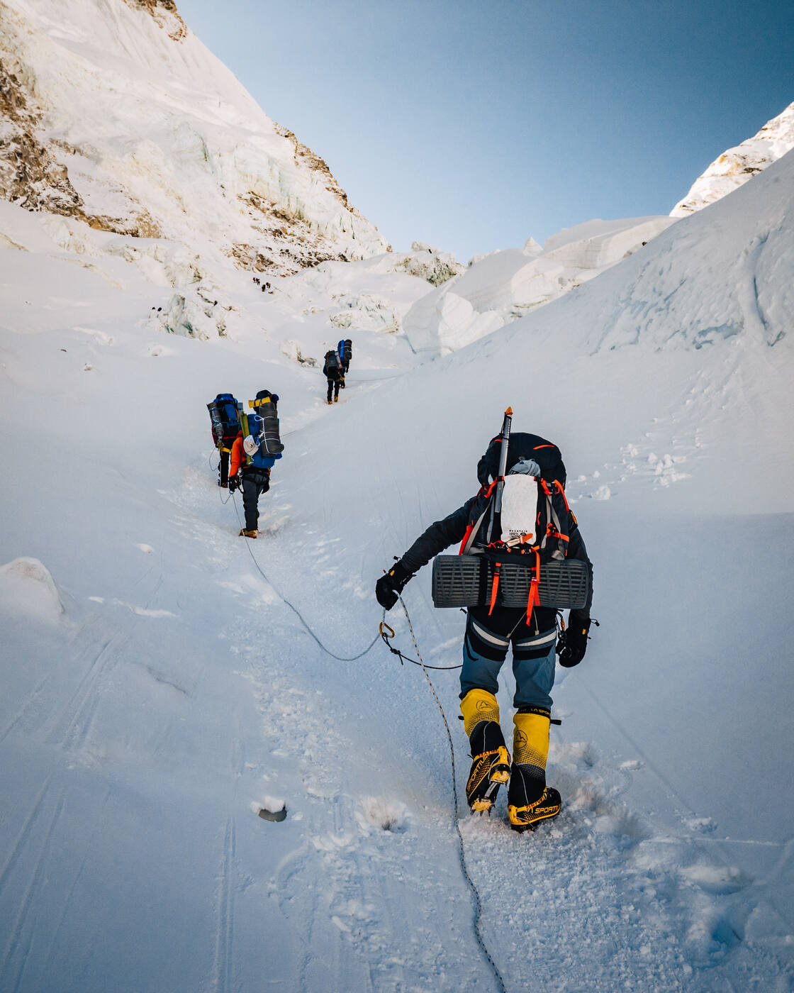 Climbers with heavy packs ascending a snow slope in the upper Icefall