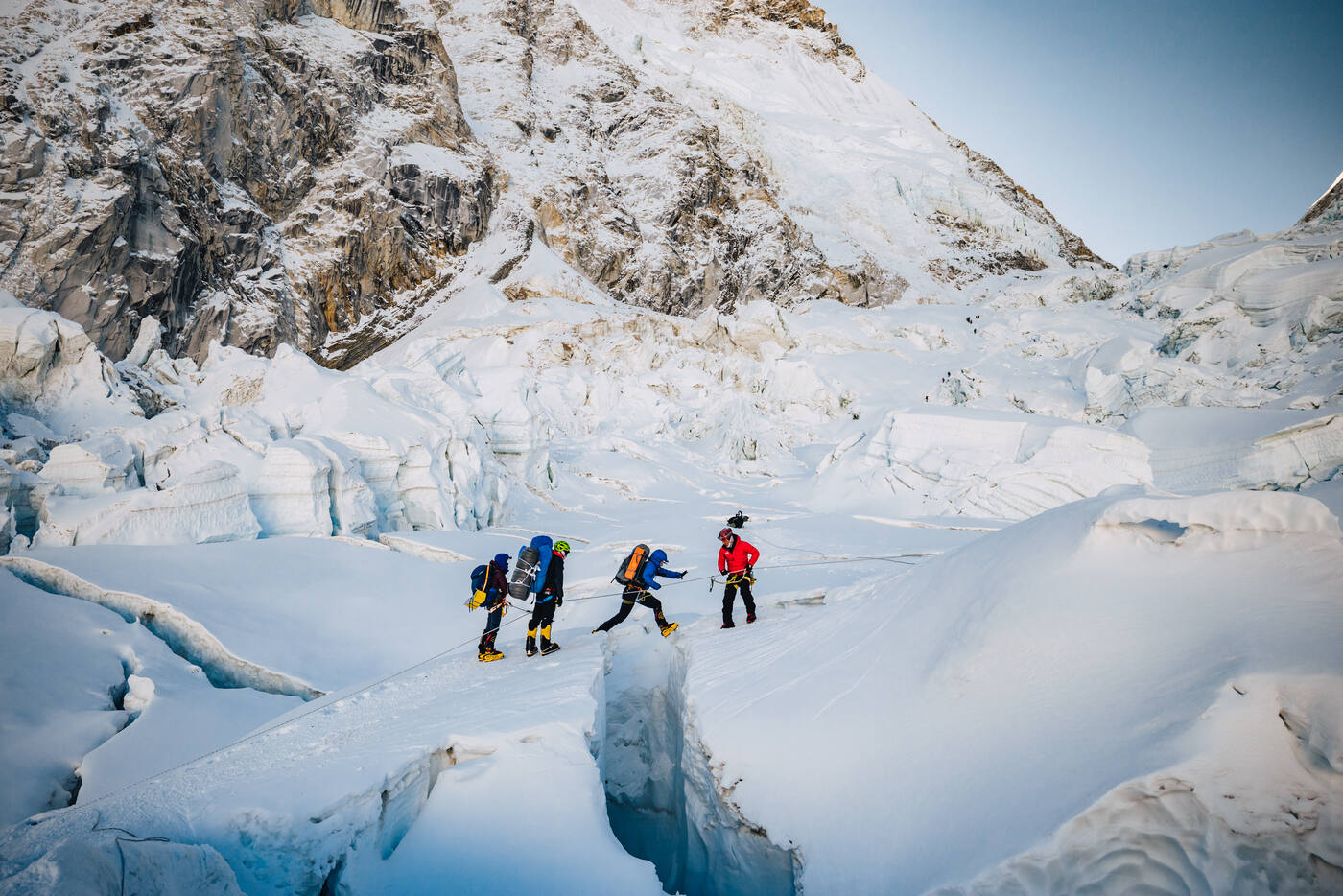 Three climbers walking among ice seracs and crevasses in the Khumbu Icefall