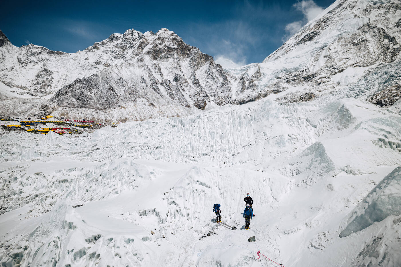 Two climbers at the base of the Khumbu Icefall with prayer flags and mountains behind